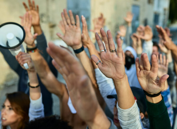 Close-up of crowd of protesters with arms raised demonstrating on the streets.